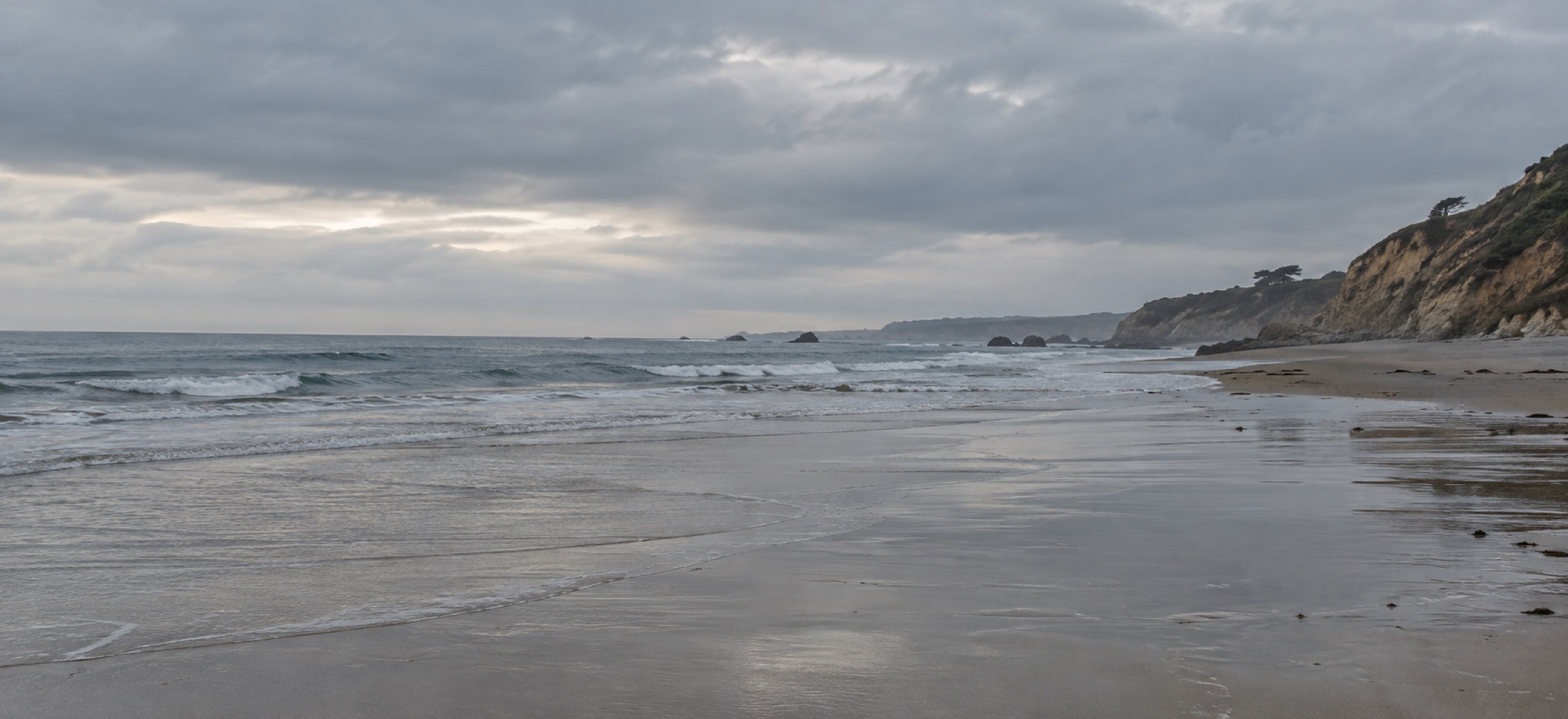 An empty beach at low tide under an overcast sky